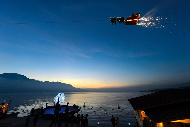 11. Ông già Noel vẫy tay với đám đông trên chiếc xe trượt tuyết trong buổi hoàng hôn ở hồ Geneva, Thụy Sĩ ngày 21/11 (Ảnh: AP)