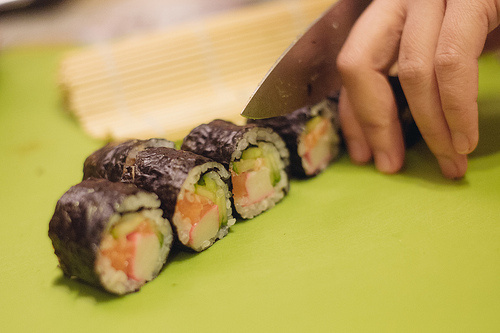 Bước 4: Đổ một chút dầu vừng ra đĩa, lăn cuộn sushi qua dầu vừng để lớp lá kim bên ngoài bóng ánh lên. Lấy một con dao sắc, xóa chút dầu ăn lên lưỡi dao để khi cắt sushi sẽ không bị dính dao. Sau đó, cắt sushi thành từng khoanh, xếp lên đĩa.